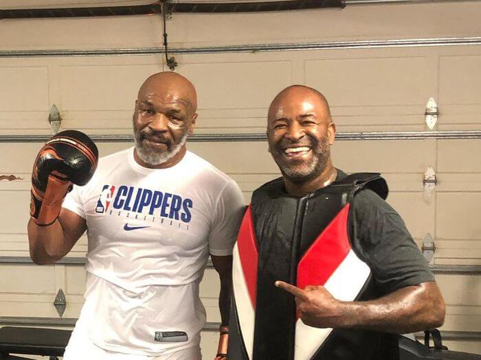Mike Tyson mengenakan sarung tinju dan kaos putih sedang berpose